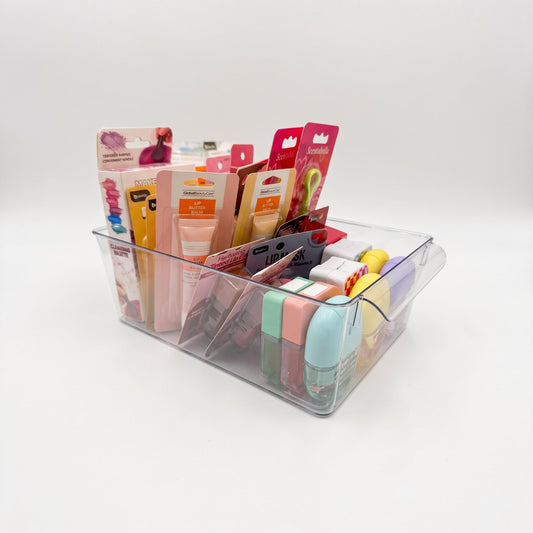 A clear plastic organizer tray holding assorted small packaged cosmetics and lip balm tubes, photographed on a clean white studio background.